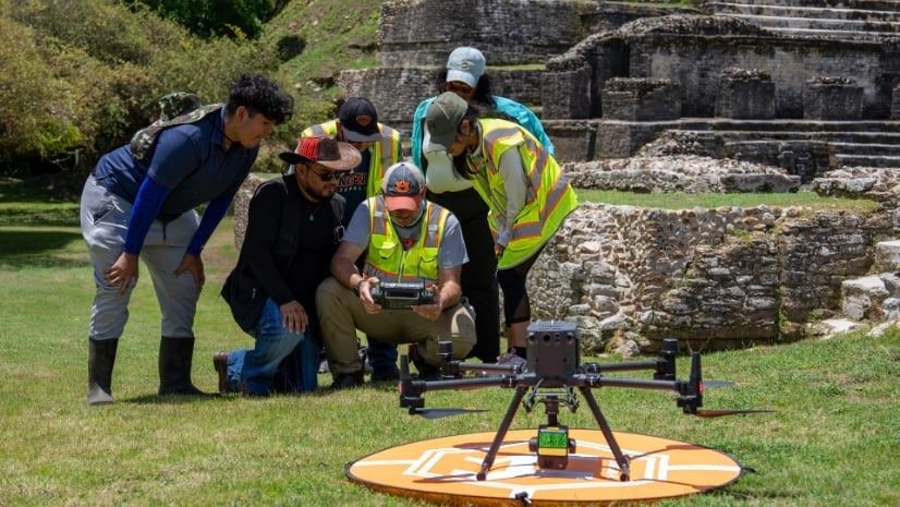 Team members review a device beside a drone at an archaeological site